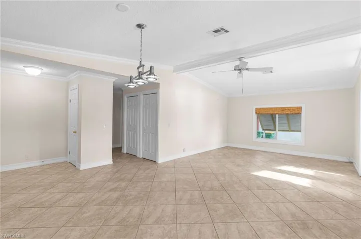 Empty room featuring crown molding, beamed ceiling, a textured ceiling, ceiling fan with notable chandelier, and light tile patterned flooring