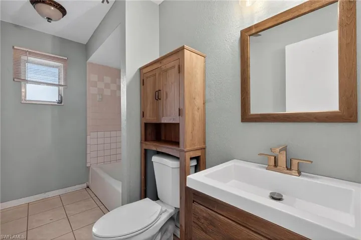 Full bath featuring vanity, light tile patterned flooring, washtub / shower combination, and a textured wall