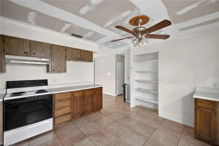 Kitchen featuring electric range, built in features, light countertops, light tile patterned floors, and wood finish cabinetry