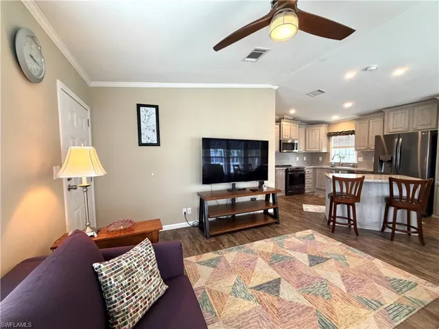 Open-concept living area with wood-finish flooring, a ceiling fan, crown molding, and recessed lighting