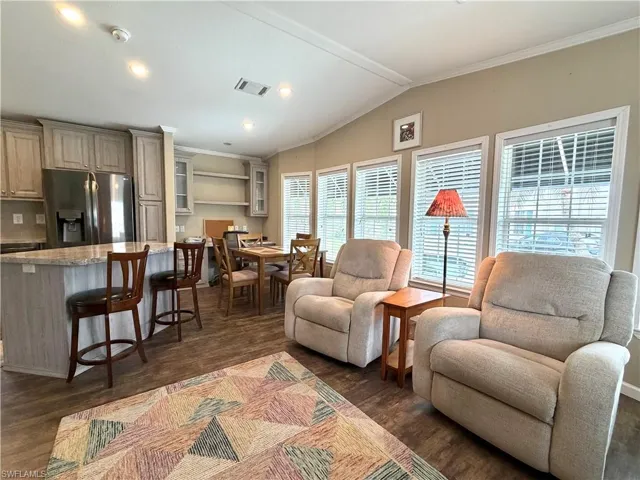 Open-concept living space with wood-finish flooring, vaulted ceilings, recessed lighting, and multiple windows with blinds