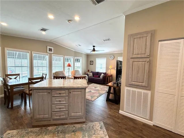 Recessed lighting, wood-finish flooring, kitchen island with stone countertop, multiple windows, and vaulted ceiling
