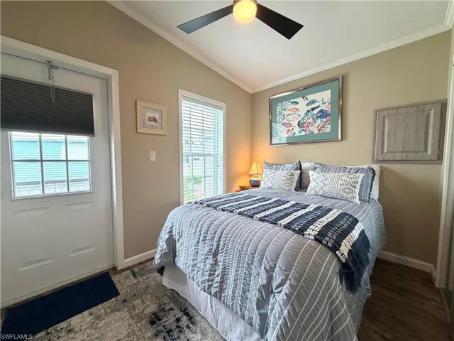 Vaulted ceiling with a ceiling fan light fixture, wood-finish flooring, white window blinds, and a paneled exterior door