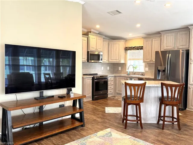 Kitchen with wood-finish flooring, recessed lighting, light-toned cabinetry, stainless steel appliances, and a central island