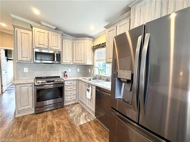 Kitchen featuring wood-finish flooring, stainless steel appliances, light-toned cabinetry, light-colored countertops, and a subway tile backsplash