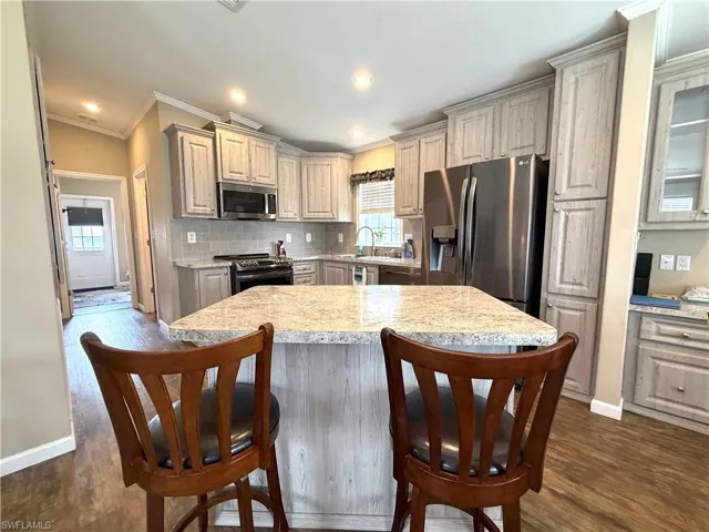 Kitchen featuring wood-finish flooring, an island with seating, stainless steel appliances, light-toned cabinetry, and a tile backsplash