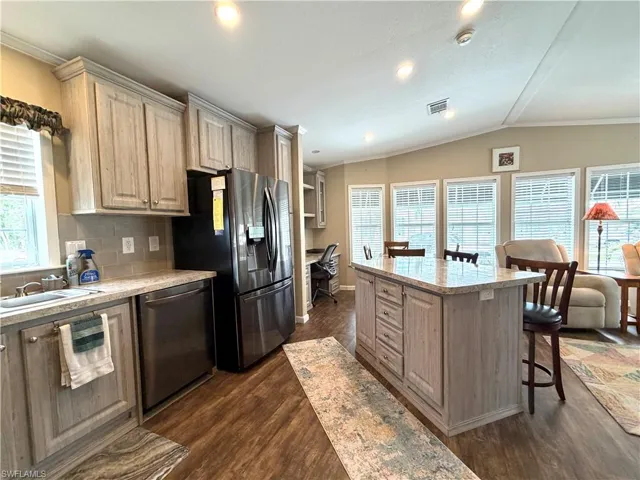 Kitchen featuring wood-finish cabinetry, stainless steel appliances, a tiled backsplash, a kitchen island with seating, and wood-finish flooring
