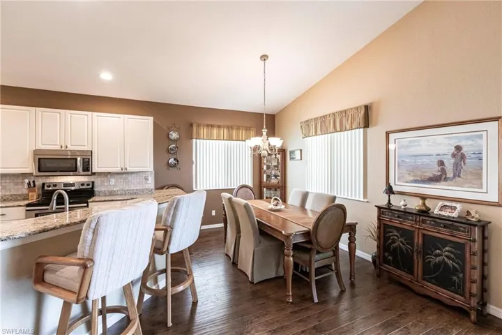 Dining room featuring dark wood-style floors, a notable chandelier, & vaulted ceiling,