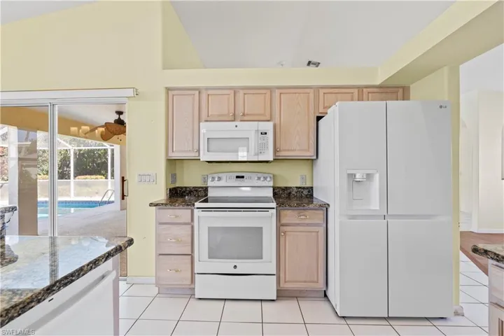 Kitchen featuring dark stone countertops, white appliances, and light brown cabinetry