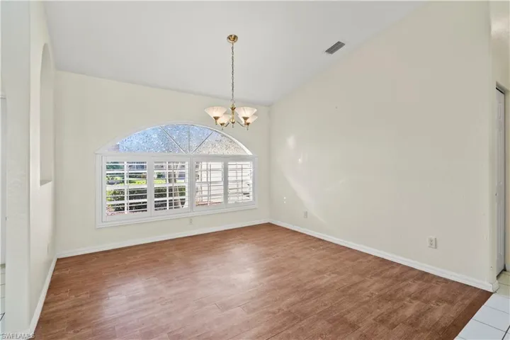 Spare room with vaulted ceiling, wood-type flooring, and an inviting chandelier