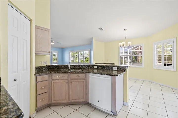 Kitchen featuring white dishwasher, ceiling fan with notable chandelier, sink, dark stone counters, and light tile patterned flooring