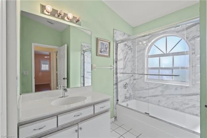 Bathroom with shower / bath combination with glass door, vanity, tile patterned floors, and lofted ceiling