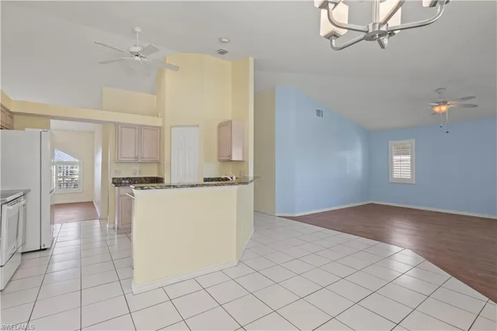 Kitchen with light tile patterned floors, light brown cabinetry, ceiling fan with notable chandelier, and white appliances