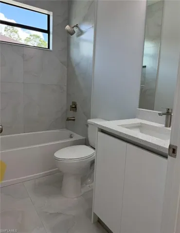 Bathroom featuring marble finish floor, tub / shower combination, toilet, and vanity