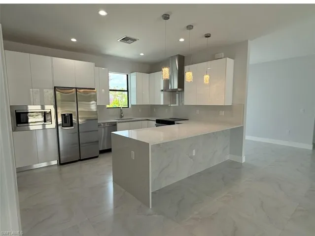 Kitchen featuring marble finish floor, visible vents, a peninsula, appliances with stainless steel finishes, and wall chimney exhaust hood