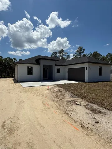View of front of property with stucco siding, a shingled roof, a garage, and dirt driveway