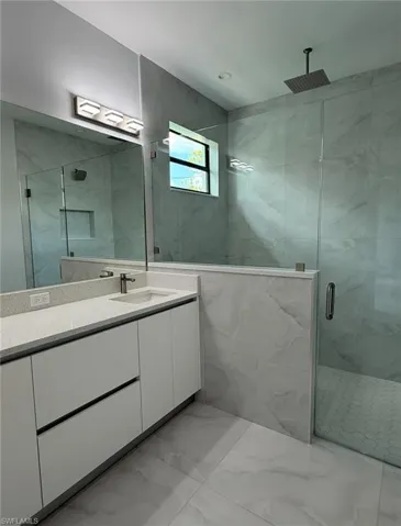 Full bathroom with tile walls, marble finish floor, a marble finish shower, and vanity
