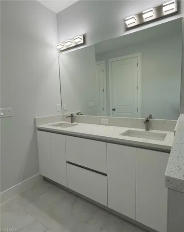 Bathroom featuring marble finish floor, a sink, double vanity, and baseboards