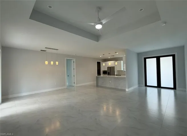 Unfurnished living room featuring a tray ceiling and baseboards
