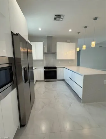 Kitchen featuring wall chimney exhaust hood, modern cabinets, stainless steel appliances, marble finish floor, and visible vents