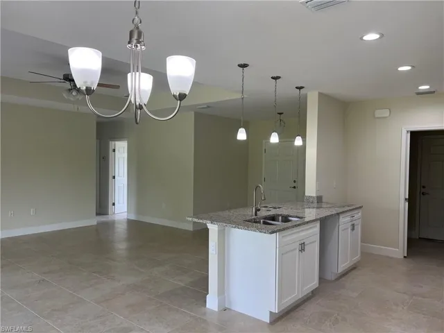 Kitchen featuring white cabinetry, light stone counters, sink, decorative light fixtures, and light tile patterned flooring