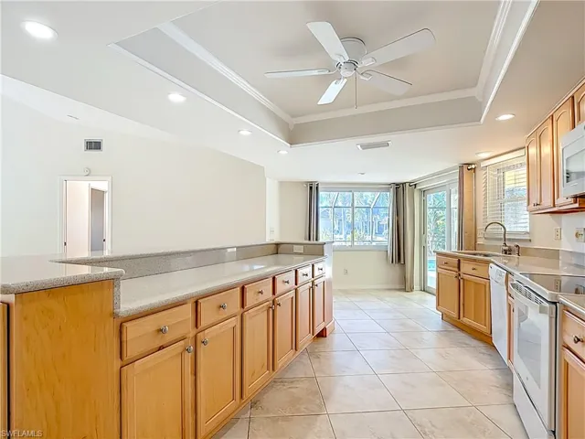 Kitchen with a raised ceiling, white appliances, ornamental molding, recessed lighting, and light tile patterned floors