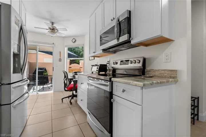 Kitchen featuring light-toned tile flooring, white shaker cabinetry, stainless steel appliances, and a granite-finish countertop
