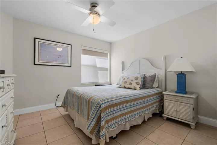 Bedroom featuring tile flooring, a window with roller shades, a ceiling fan with light fixture, and a louvered headboard