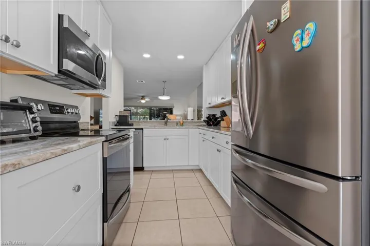 Modern kitchen with stainless steel appliances, white cabinetry, light-toned countertops, and tile flooring