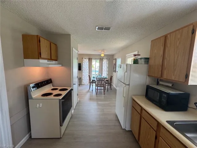 Kitchen featuring white appliances, brown cabinetry, light countertops, light wood-style flooring, and a textured ceiling