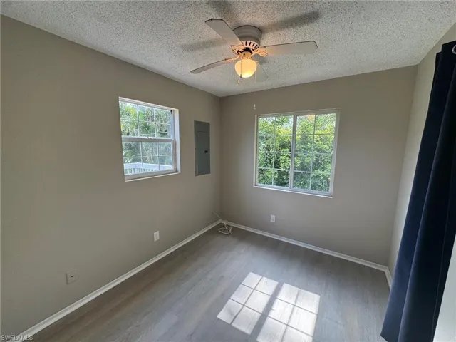 Empty room with wood finished floors, a textured ceiling, electric panel, and ceiling fan