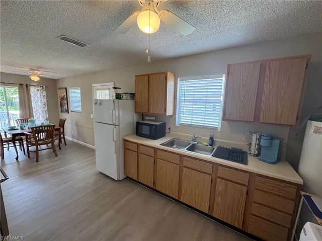 Kitchen with a ceiling fan, light wood-style floors, light countertops, freestanding refrigerator, and plenty of natural light