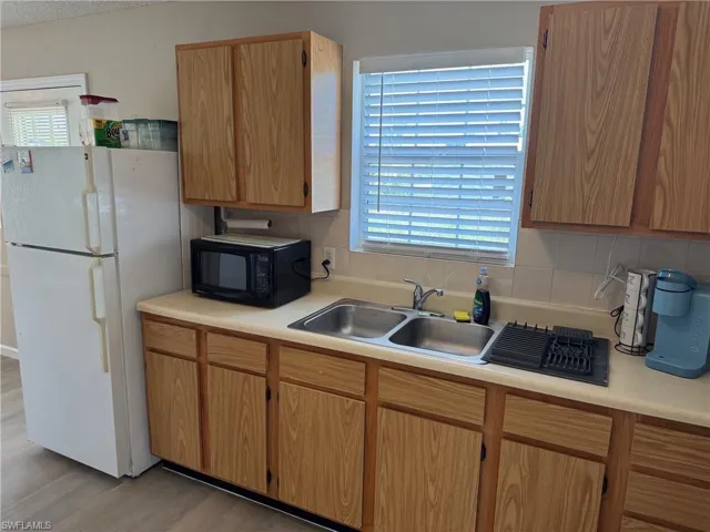 Kitchen featuring freestanding refrigerator, light countertops, black microwave, and decorative backsplash