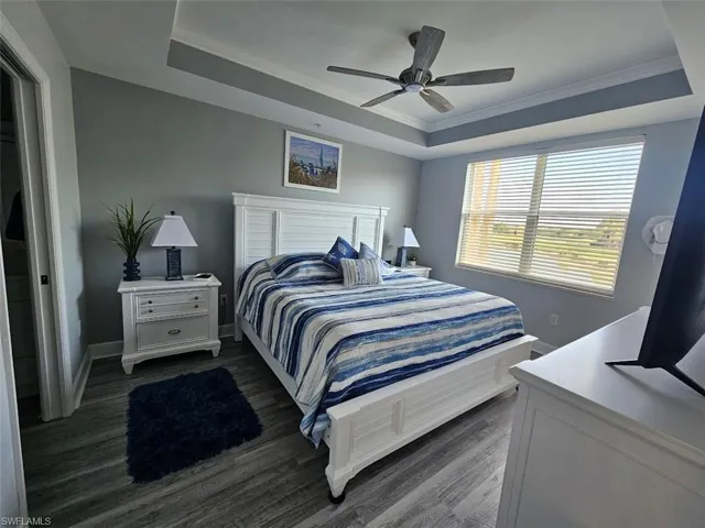 Bedroom featuring a tray ceiling, dark wood finished floors, a ceiling fan, and ornamental molding