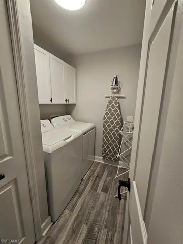 Washroom featuring dark wood-type flooring, washing machine and clothes dryer, baseboards, and cabinet space