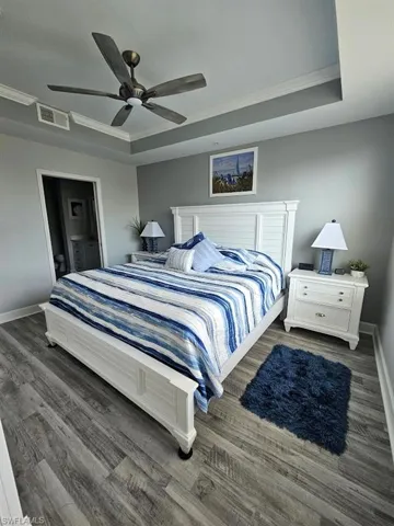 Bedroom featuring visible vents, baseboards, a raised ceiling, crown molding, and wood finished floors