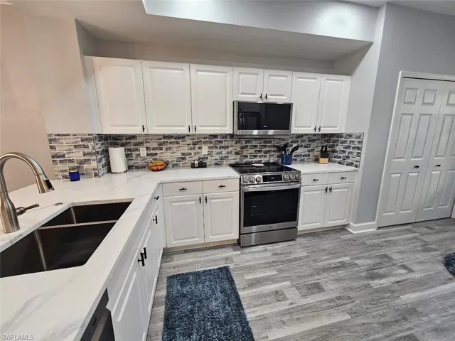 Kitchen with a sink, white cabinetry, stainless steel appliances, backsplash, and light wood-style flooring