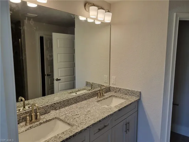 Bathroom featuring double vanity, a textured wall, and a tile shower