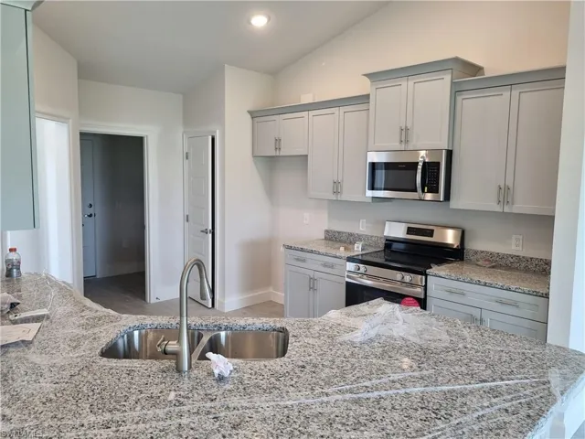 Kitchen featuring appliances with stainless steel finishes, a sink, light stone countertops, gray cabinetry, and recessed lighting