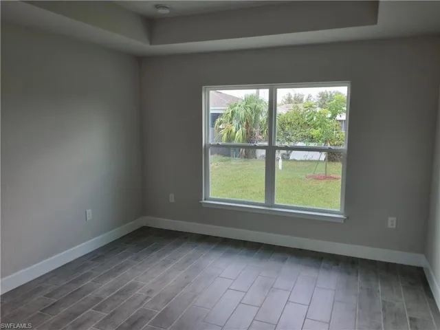 Empty room with baseboards, wood finished floors, and a raised ceiling