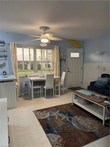 Living room with radiator heating unit, light tile patterned floors, ceiling fan, and a wainscoted wall