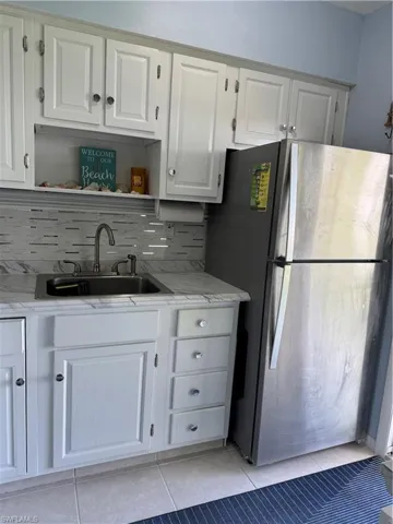 Kitchen with refrigerator, open shelves, light tile patterned flooring, white cabinetry, and decorative backsplash