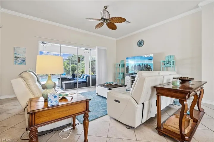 Living room featuring ornamental molding, light tile patterned flooring, and ceiling fan