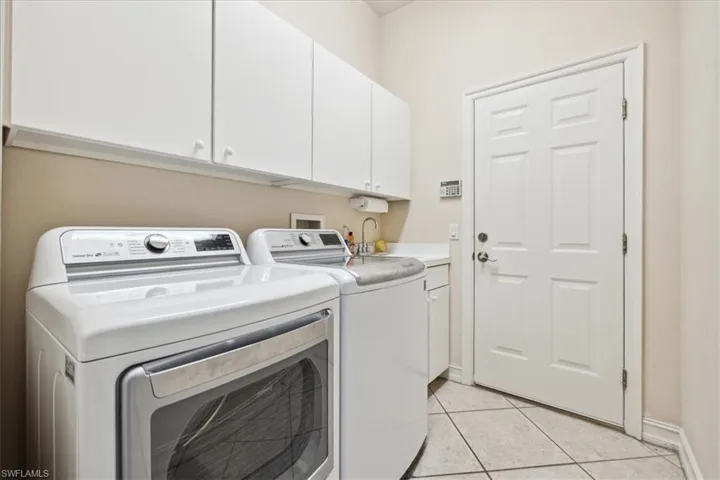Clothes washing area featuring light tile patterned flooring, sink, independent washer and dryer, and cabinets