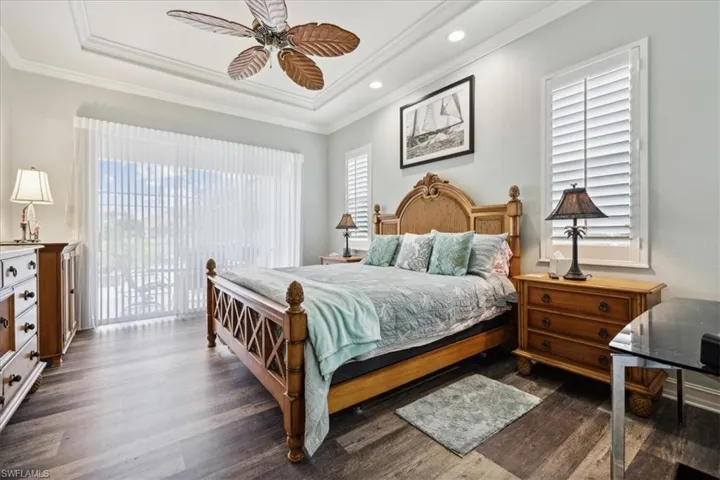 Bedroom featuring multiple windows, access to outside, dark wood-type flooring, ceiling fan, and a raised ceiling