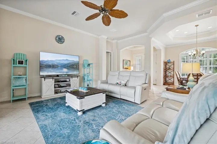 Tiled living room with ornamental molding, ceiling fan with notable chandelier, and a tray ceiling
