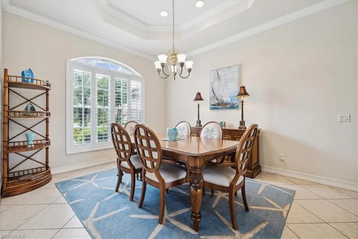 Tiled dining area with ornamental molding, a chandelier, and a tray ceiling