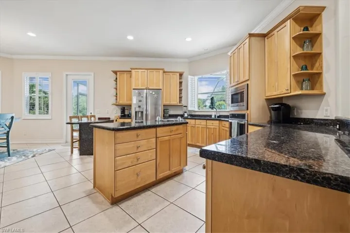 Kitchen with dark stone counters, light brown cabinets, appliances with stainless steel finishes, and light tile patterned floors