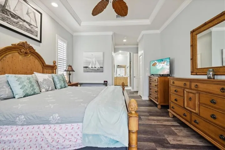 Bedroom featuring connected bathroom, crown molding, dark wood-type flooring, ceiling fan, and a raised ceiling