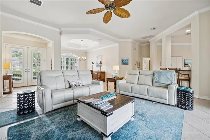 Tiled living room with ceiling fan with notable chandelier, crown molding, french doors, and a tray ceiling